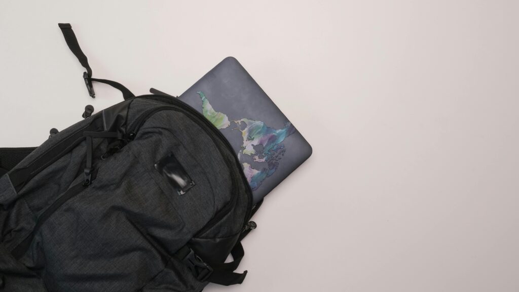 Flat lay of a backpack with a laptop featuring a colorful artistic cover, perfect for travel or everyday use.