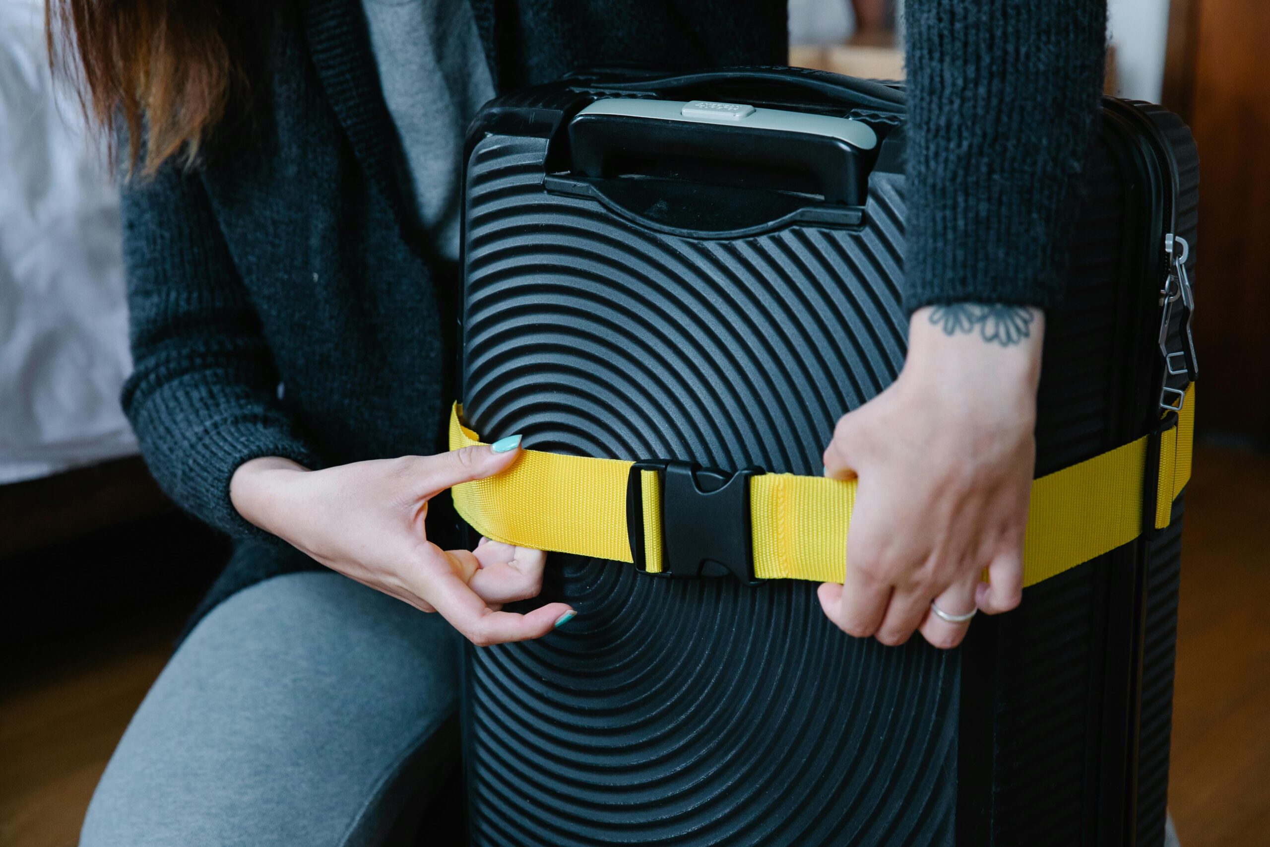 Close-up of hands fastening a bright yellow strap around a black suitcase.