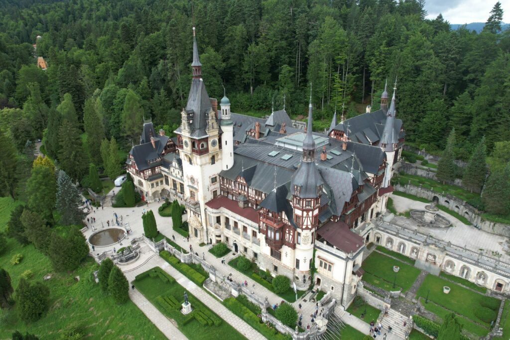 Stunning aerial photograph of Peles Castle surrounded by lush forests in Romania.