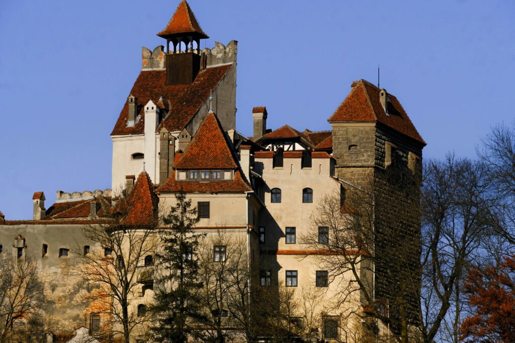 Stunning view of Bran Castle with red roofs and barren trees under a clear blue sky.