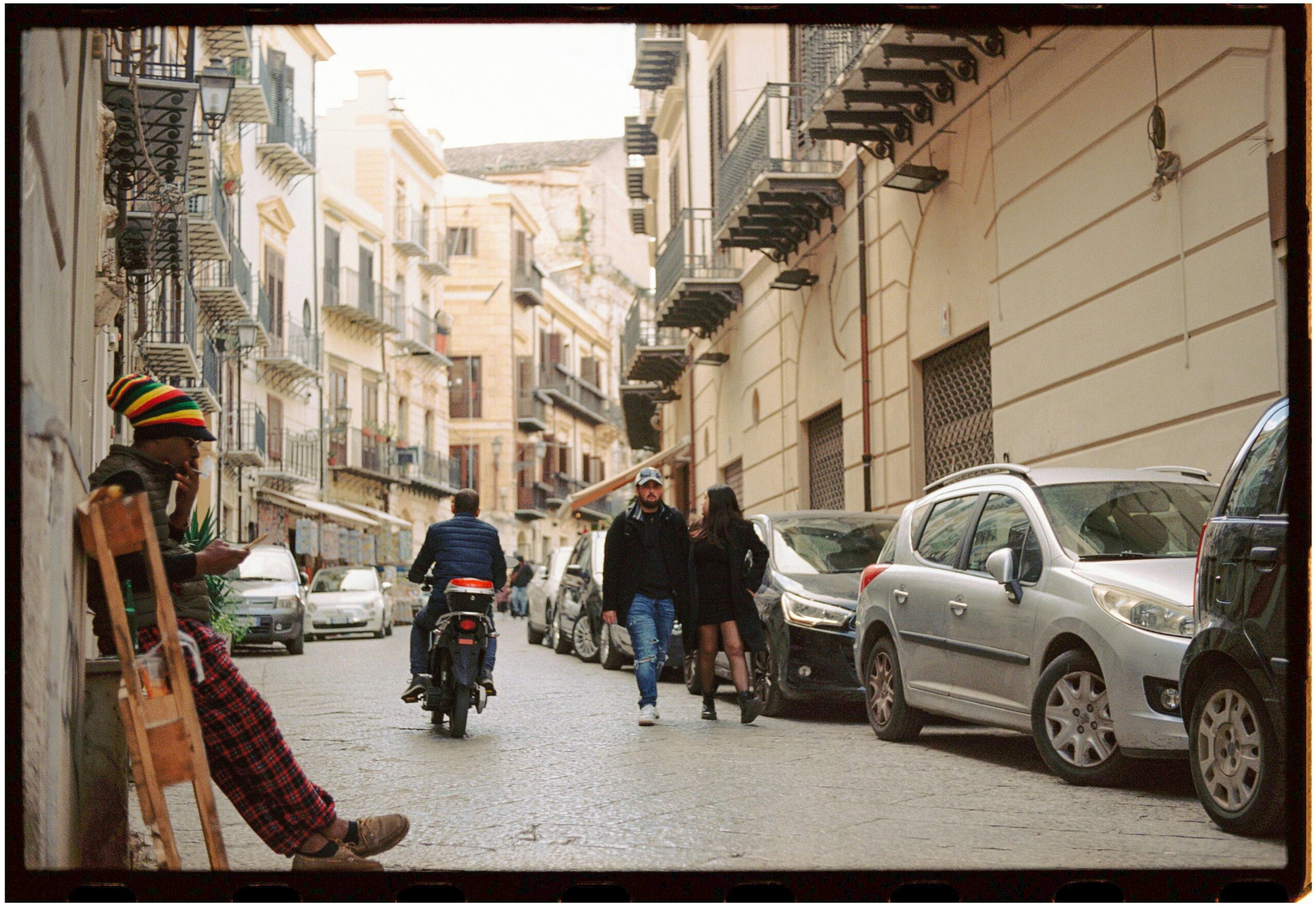 Charming urban street in Palermo with pedestrians, vehicles, and classic architecture.