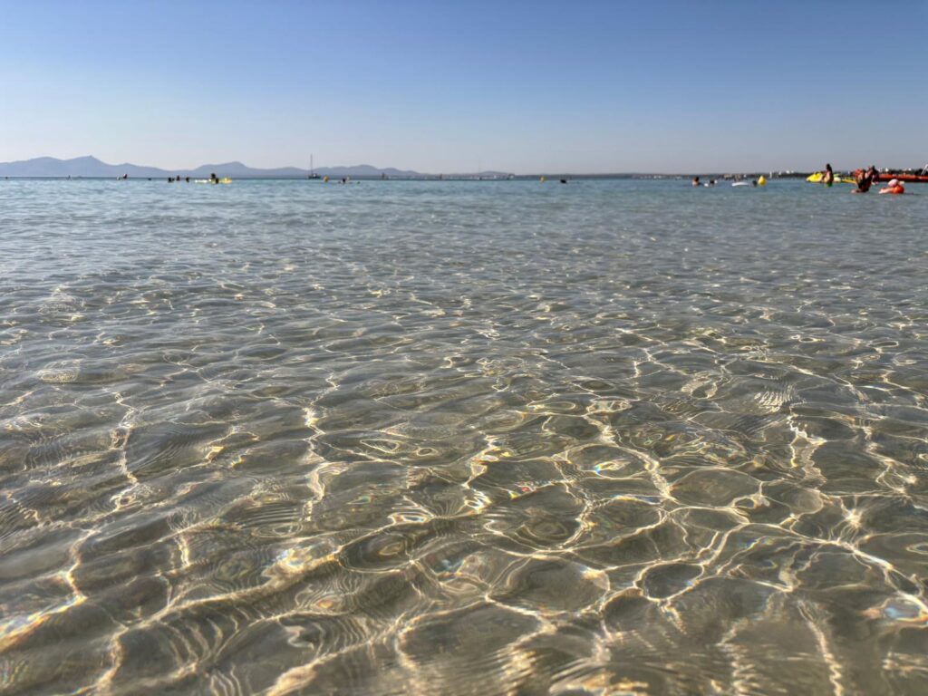 Shallow clear water at Alcudia Beach Mallorca with kids in distance